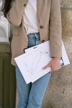 A person in casual business attire holding financial documents with graphs, indoors.