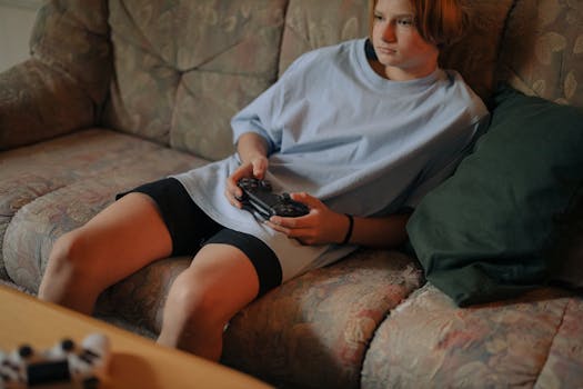 Teen wearing casual clothes playing video games on the sofa with a controller in a cozy living room setting.