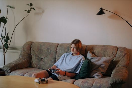 A teenager sitting on a sofa in a living room, focused on playing video games.