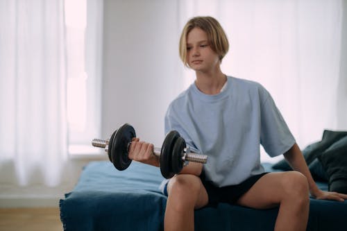 A Young Man Sitting on the Bed while Holding a Barbell