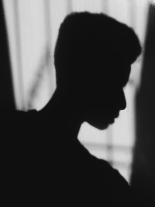 Black and white side view of anonymous desperate ethnic male silhouette at home on blurred background