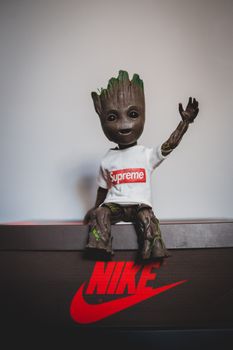 Creative popular collectible toy in stylish white t shirt with raised arm placed on black box with inscription on white background