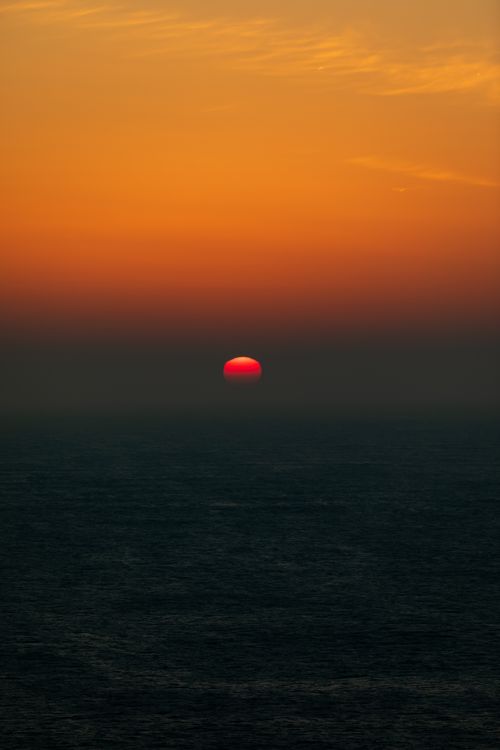 Free A stunning ocean sunset with a vibrant red sun setting on the horizon, creating a vivid seascape. Stock Photo