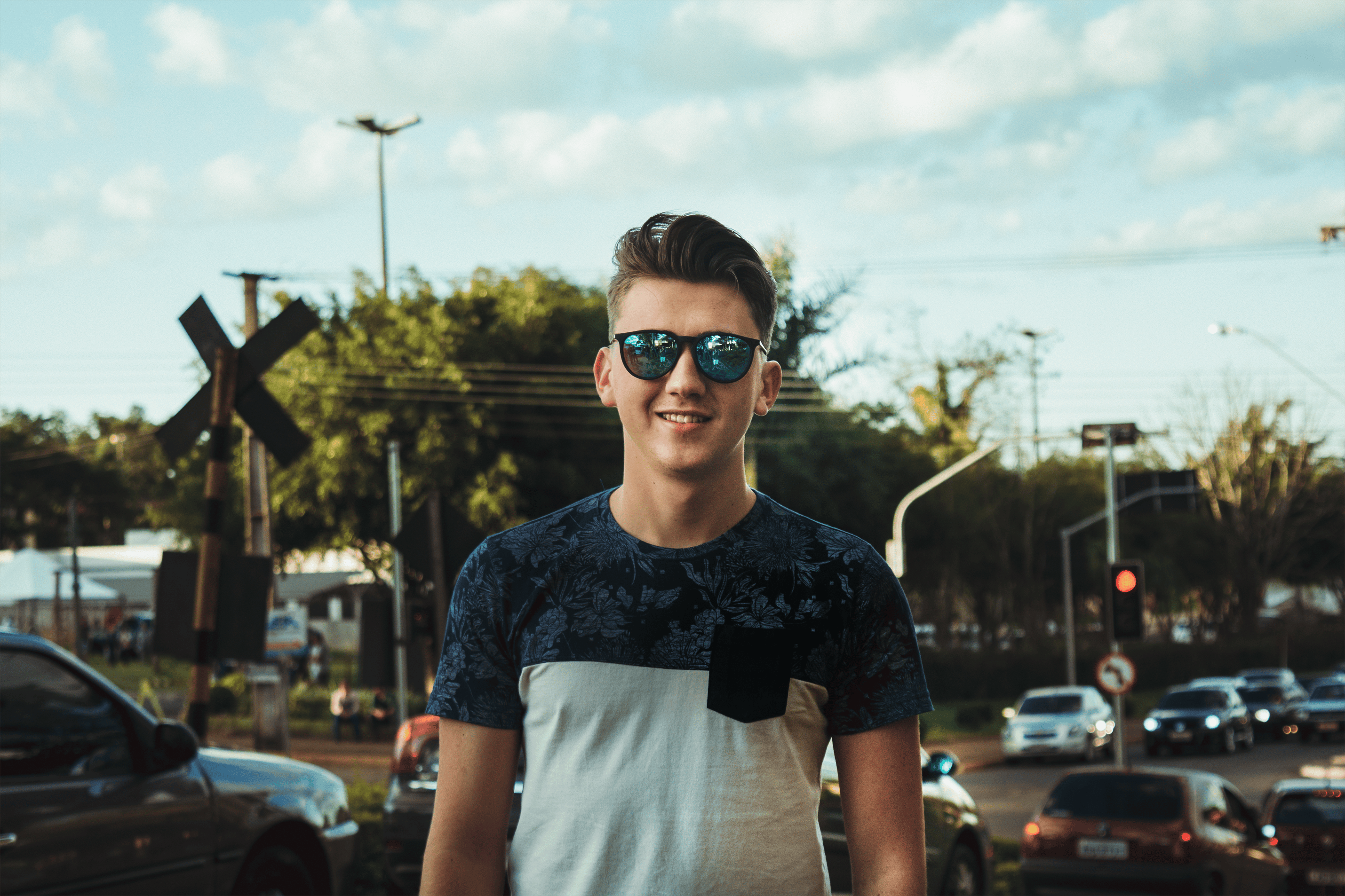 Portrait of a young man wearing sunglasses in a lively urban setting, showcasing casual style.