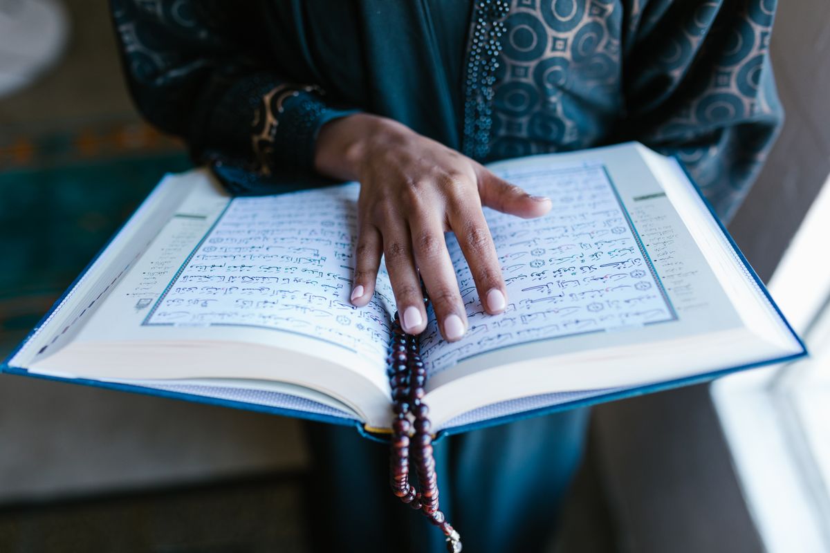 Hands holding open Quran book during careful Islamic study and Noorani Qaida practice