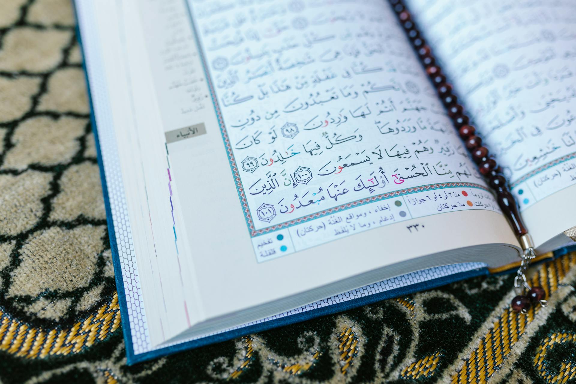 An open Quran with prayer beads rests on a beautifully designed Islamic prayer mat.