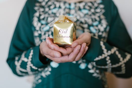 Close-up of a person holding a golden Eid Mubarak gift wrapped with a white ribbon.