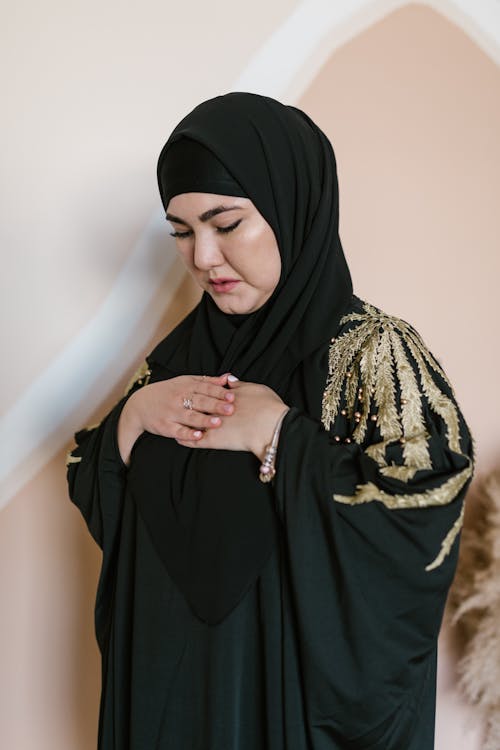 A Woman in Black Hijab Praying with Hands on Chest