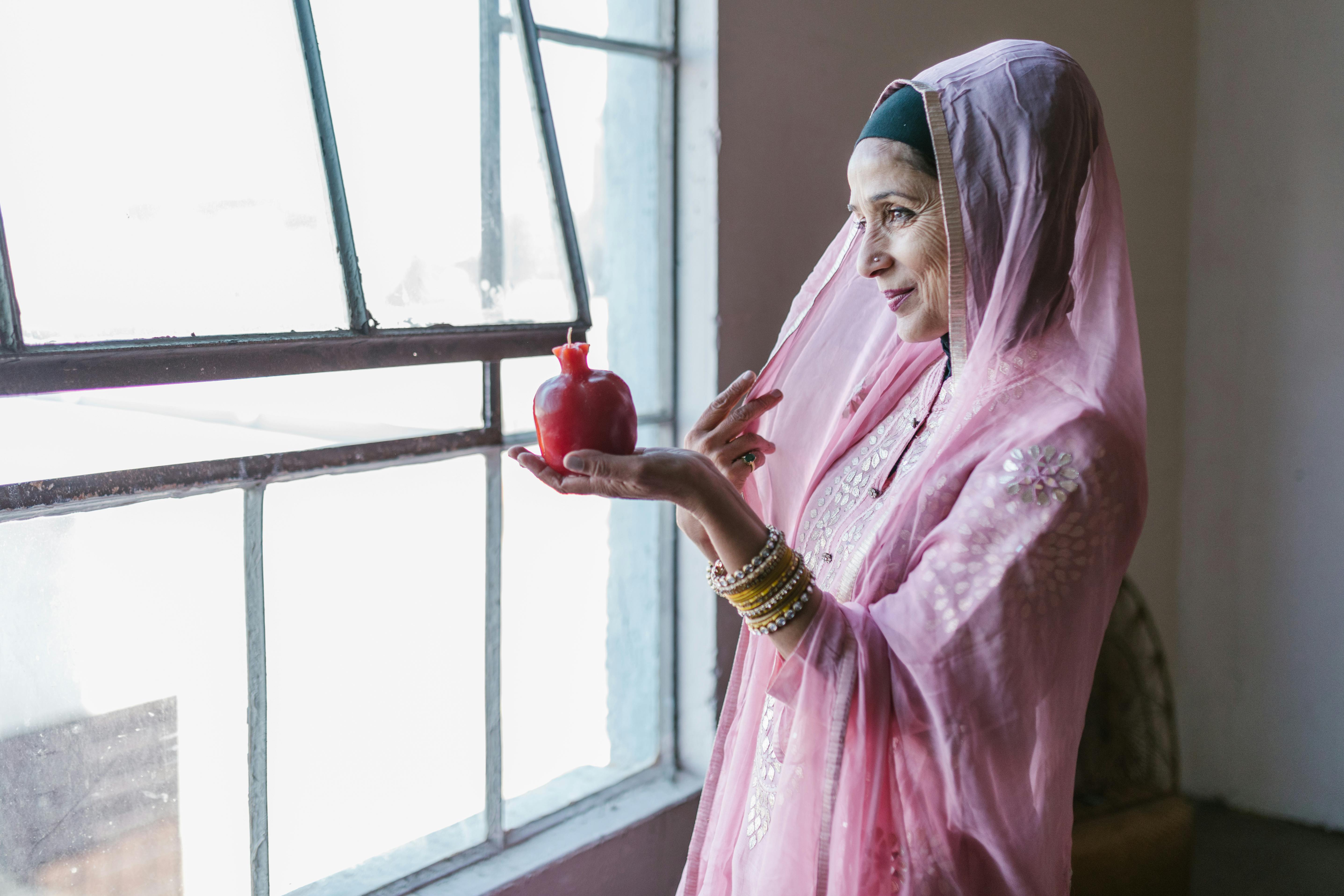 woman in pink and white floral dress wearing blue hijab holding red glass bottle