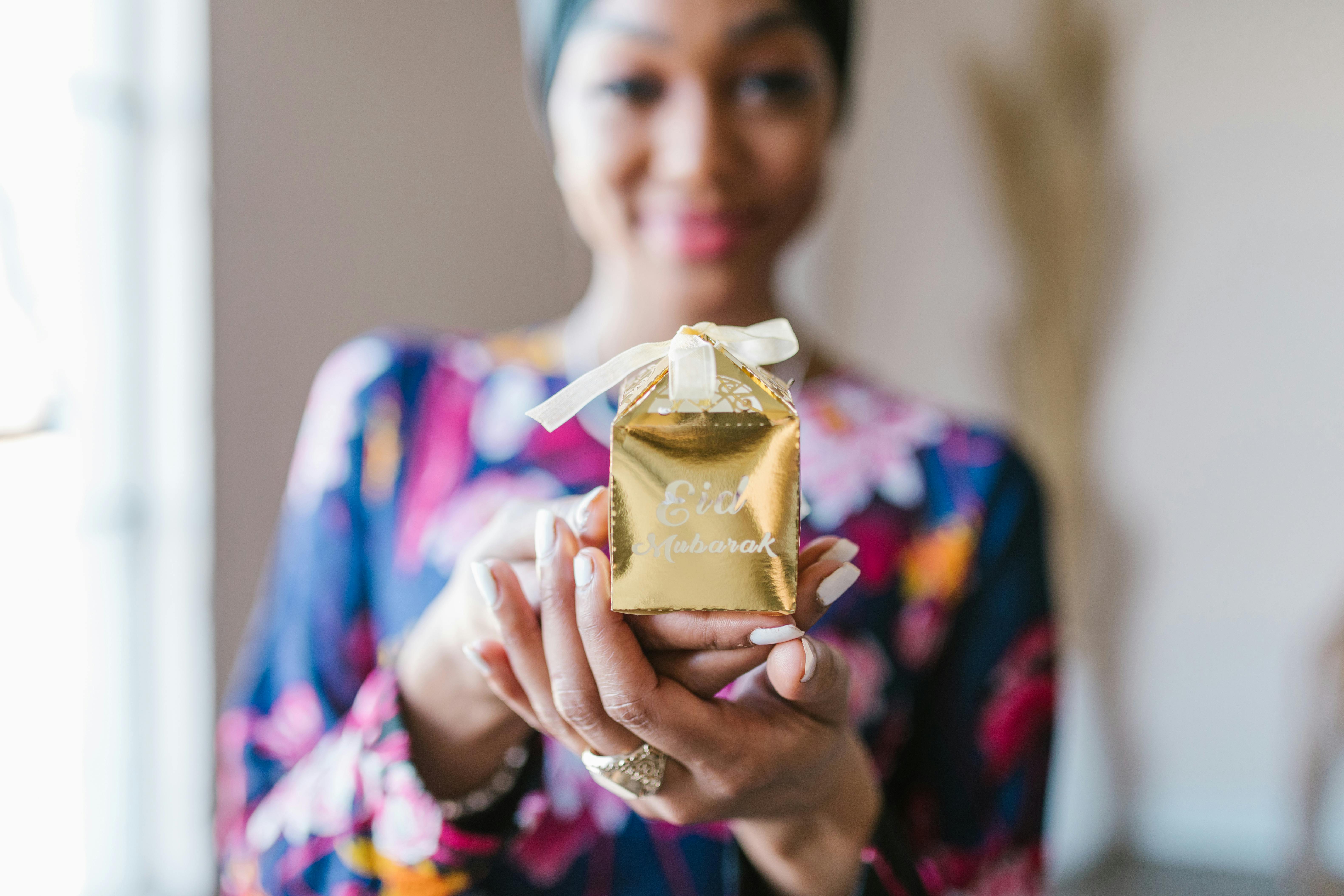 woman in blue and pink floral dress holding gold gift box