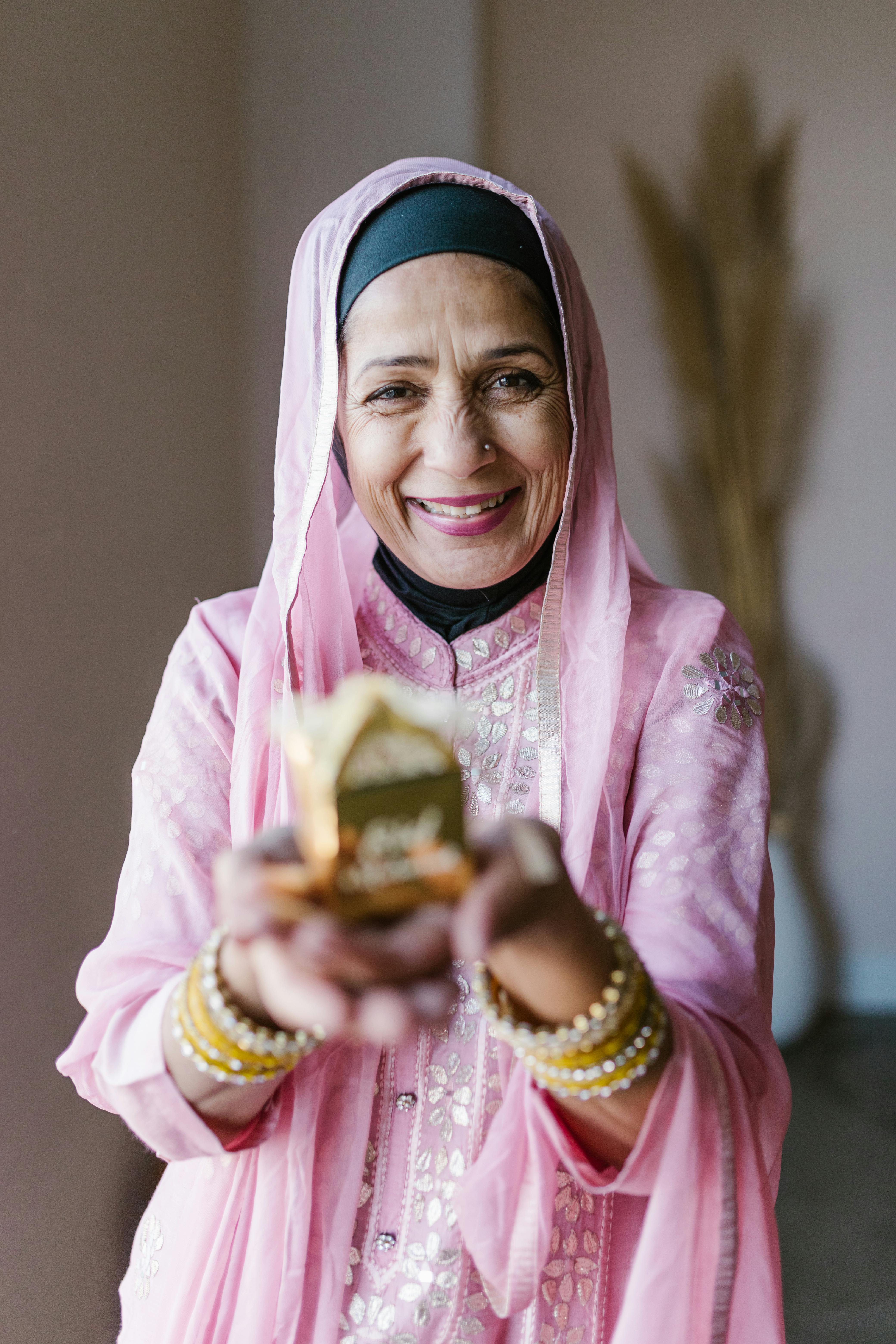 smiling woman in pink and white hijab holding gold and gold trophy