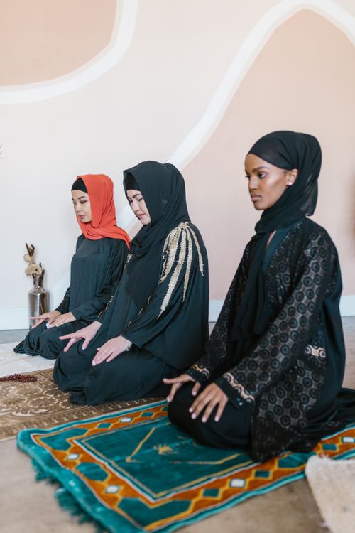 Free Three women wearing hijabs kneeling on prayer rugs, engaging in Islamic prayer. Stock Photo