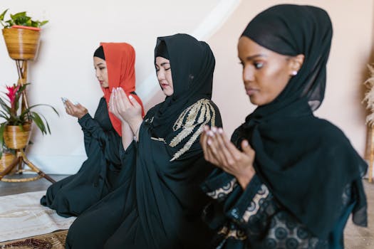A serene scene of three women in hijabs praying indoors, reflecting Islamic faith and modest fashion.