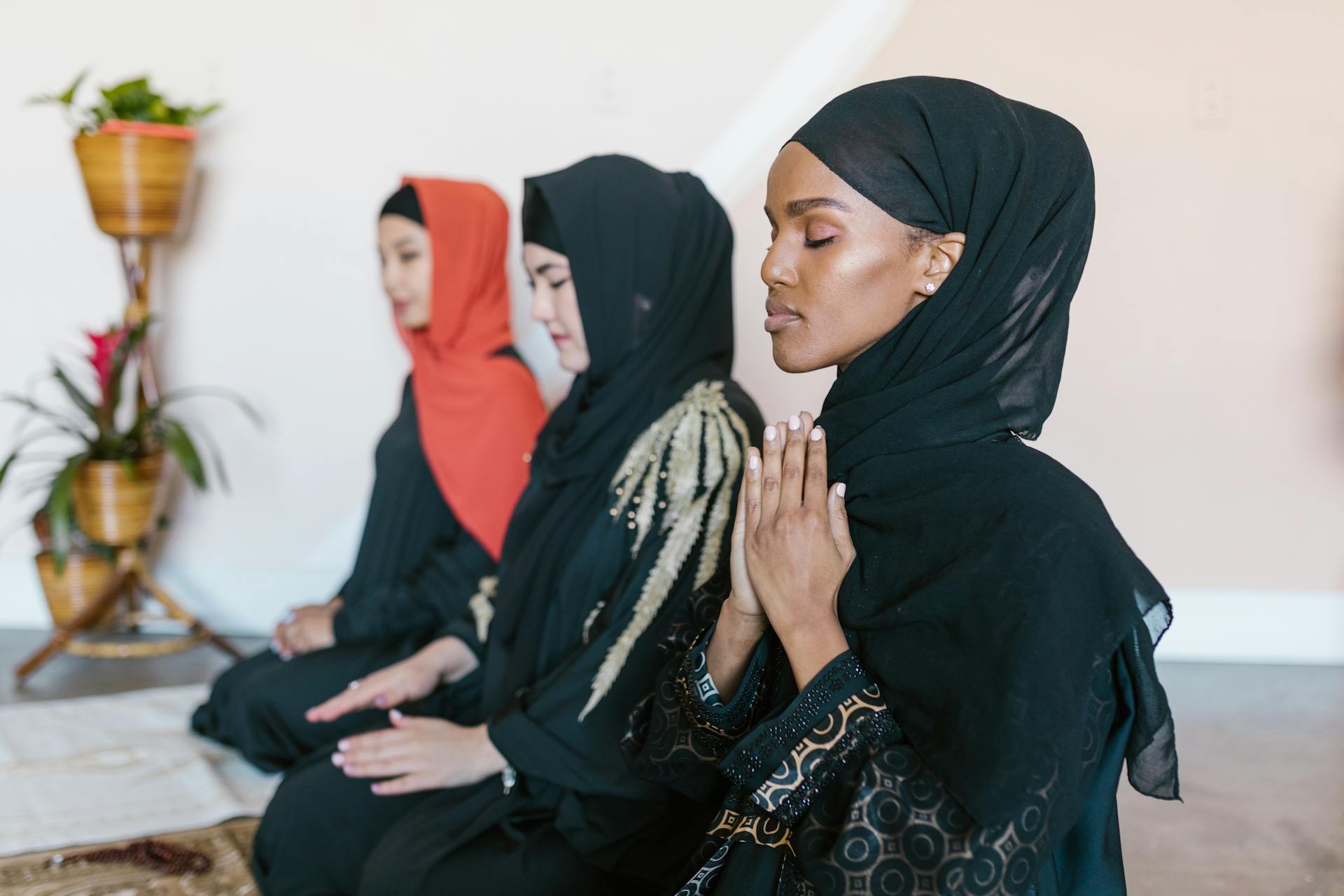 Three women in hijabs praying indoors, embodying Islamic faith and tradition.