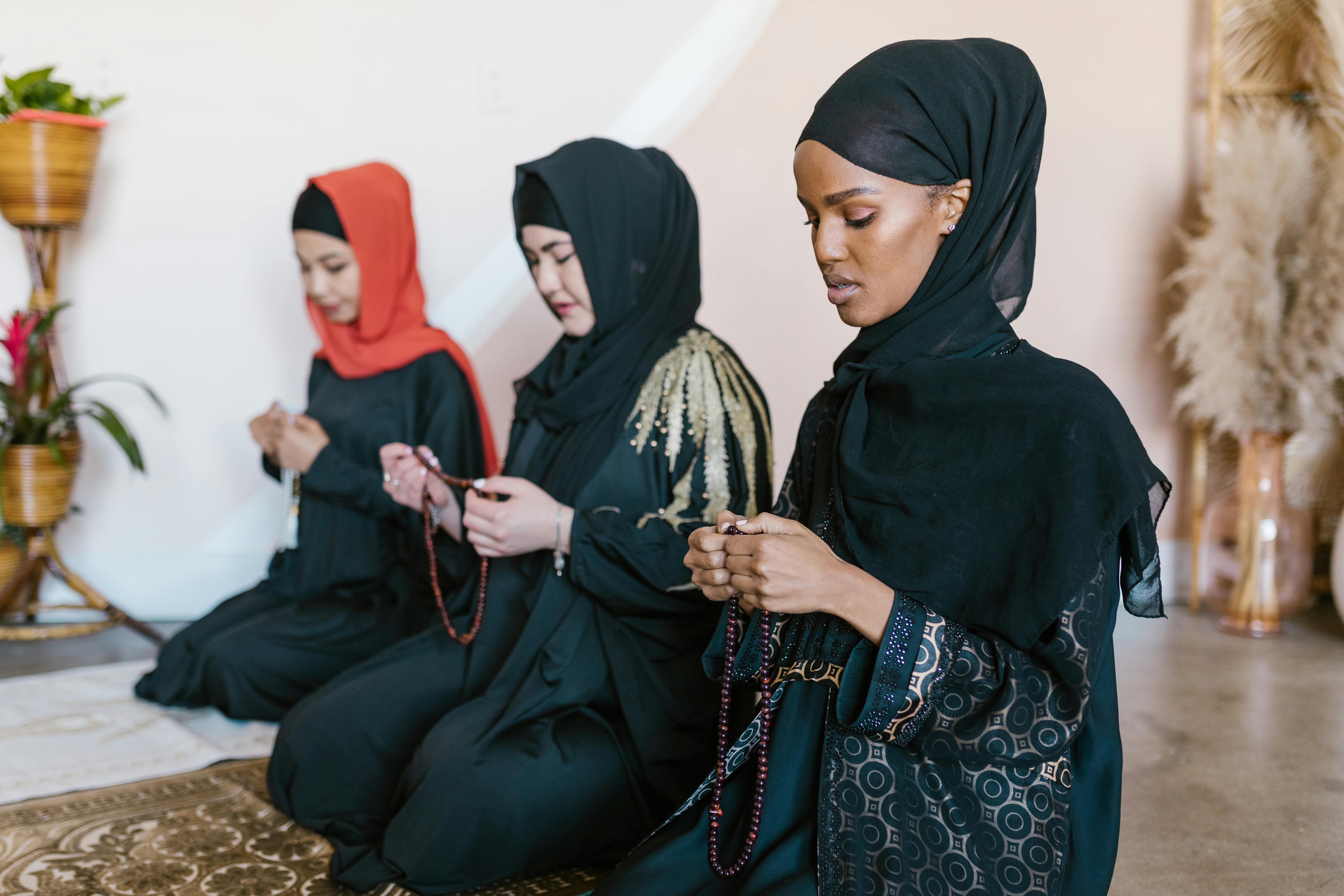 3 women wearing hijab sitting on brown carpet