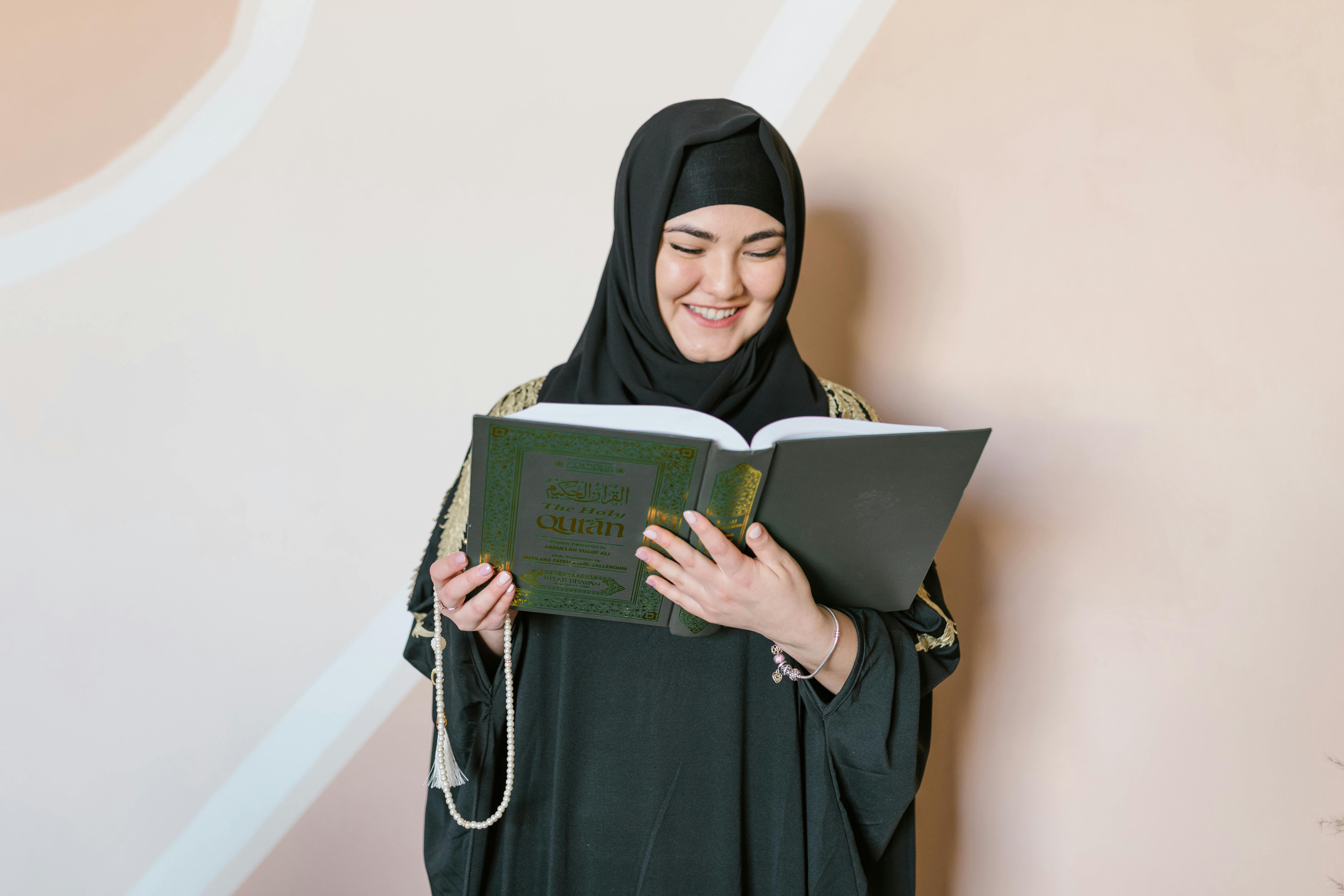 woman in black hijab holding green book