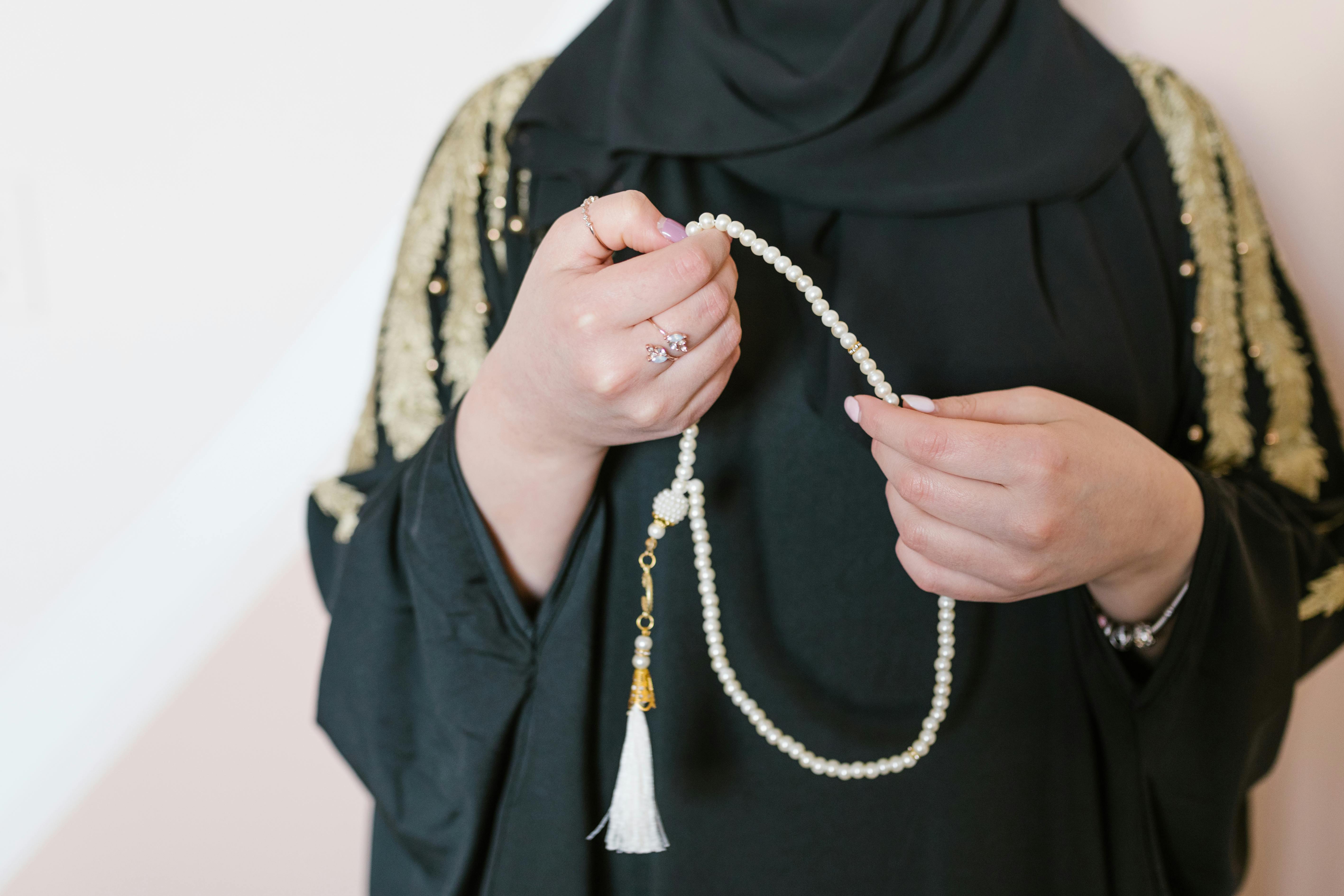 person in black hijab holding white beaded necklace