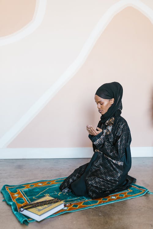 Woman in Black Abaya and Hijab Kneeling on Rug