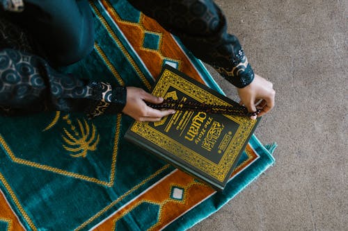 Free Hands of a Person Holding a Prayer Beads on a Book Stock Photo