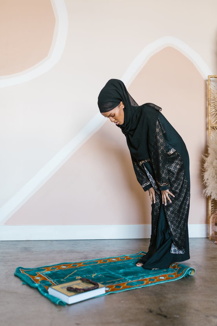 Woman In Black Hijab Bowing On A Prayer Rug