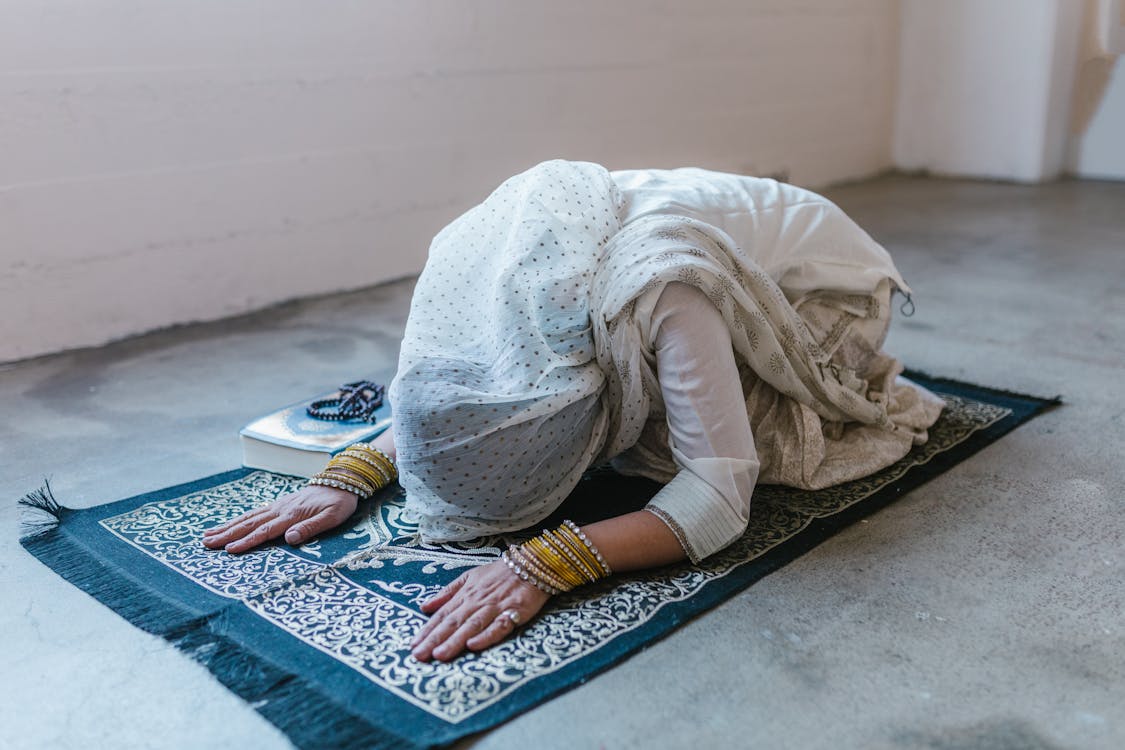 Free A Woman Wearing a White Headscarf Bowing Down on a Prayer Rug Stock Photo