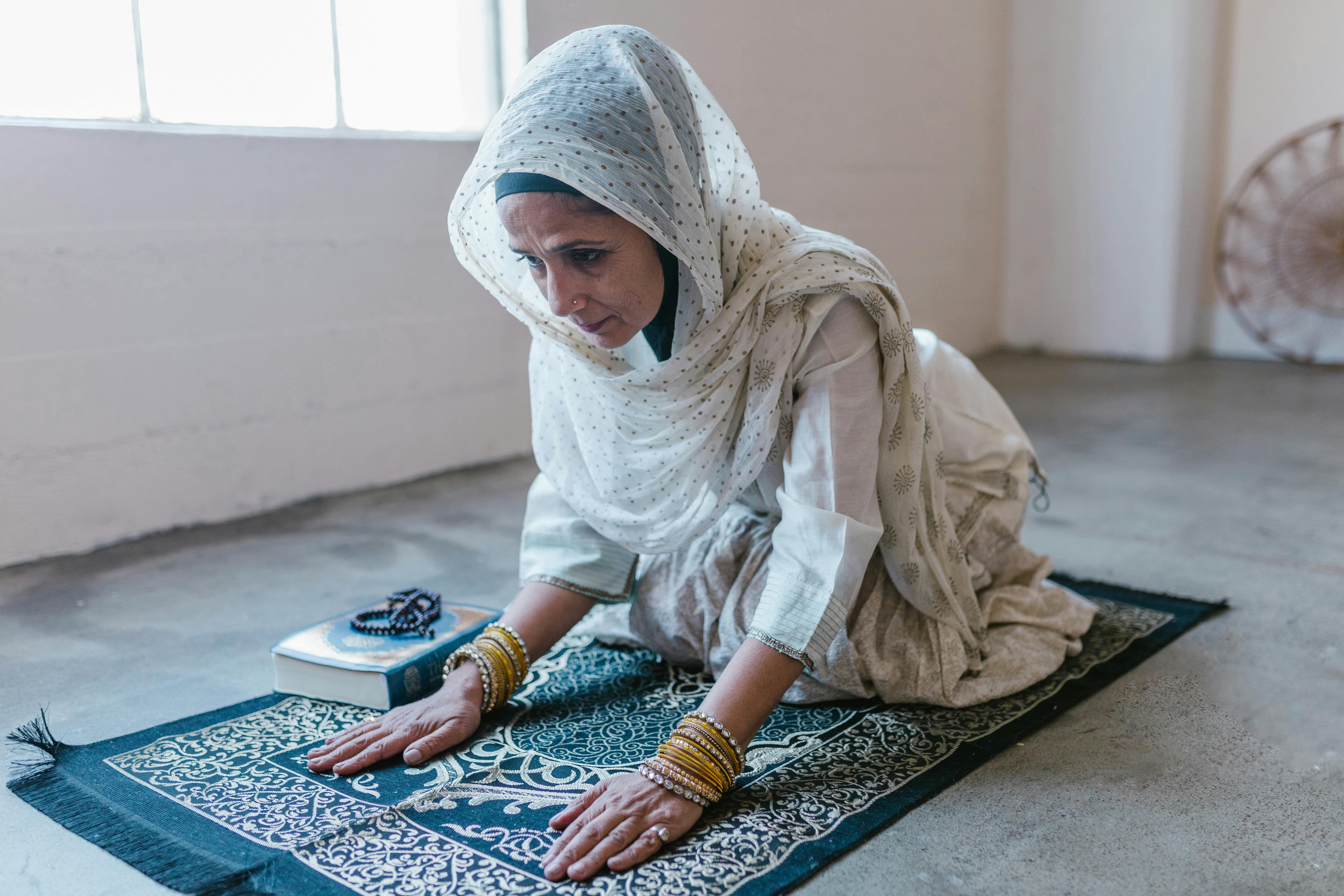 woman in white hijab sitting on blue and white rug