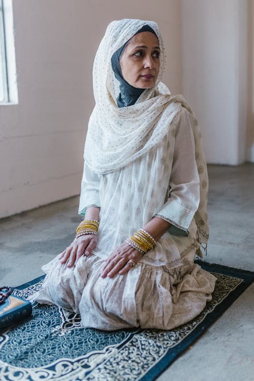 An Woman in Printed Headscarf Kneeling on a Prayer Rug