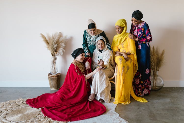 A Group Of Women In Dresses Wearing Hijabs Looking At A Cellphone