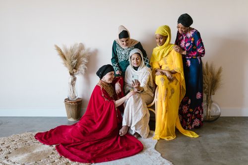 Free A diverse group of women in colorful hijabs gathered indoors, sharing a cellphone together. Stock Photo