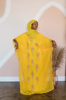Stylish woman in a vibrant yellow traditional dress posing gracefully indoors.