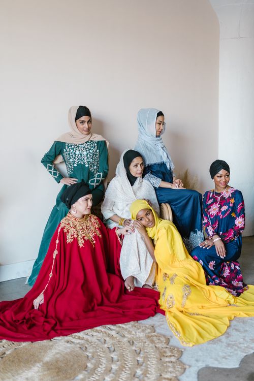 Free A group of women in colorful traditional dresses and hijabs, sitting together indoors. Stock Photo