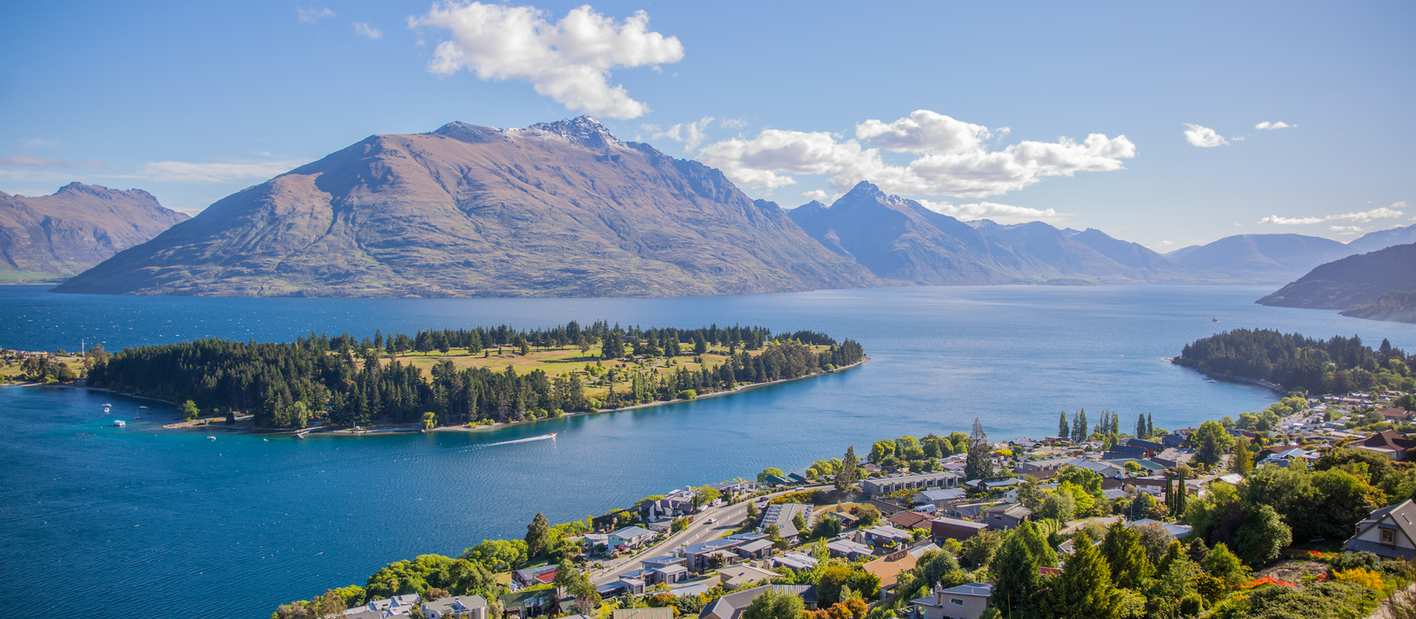 Breathtaking aerial view of Queenstown by Lake Wakatipu, surrounded by majestic mountains under clear skies. — flights from Auckland to Queenstown