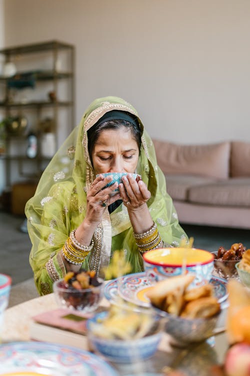 Woman in Green Hijab Drinking on a Ceramic Bowl