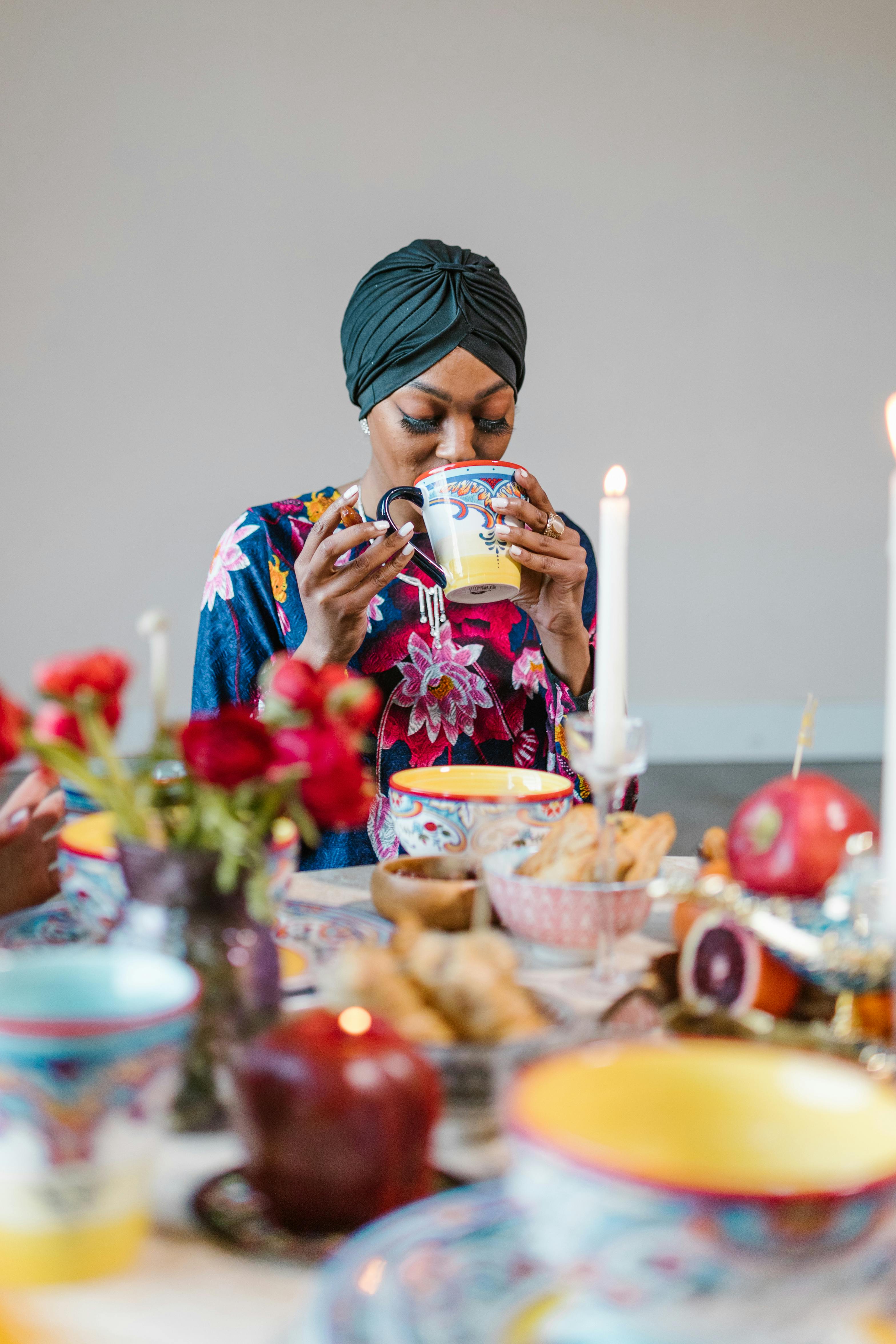 A woman in a colorful hijab enjoys a festive meal with vibrant tableware and flowers.