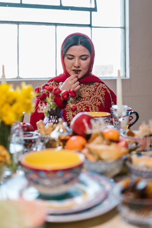 Free Woman in Red Hijab and Traditional Clothing Eating Stock Photo