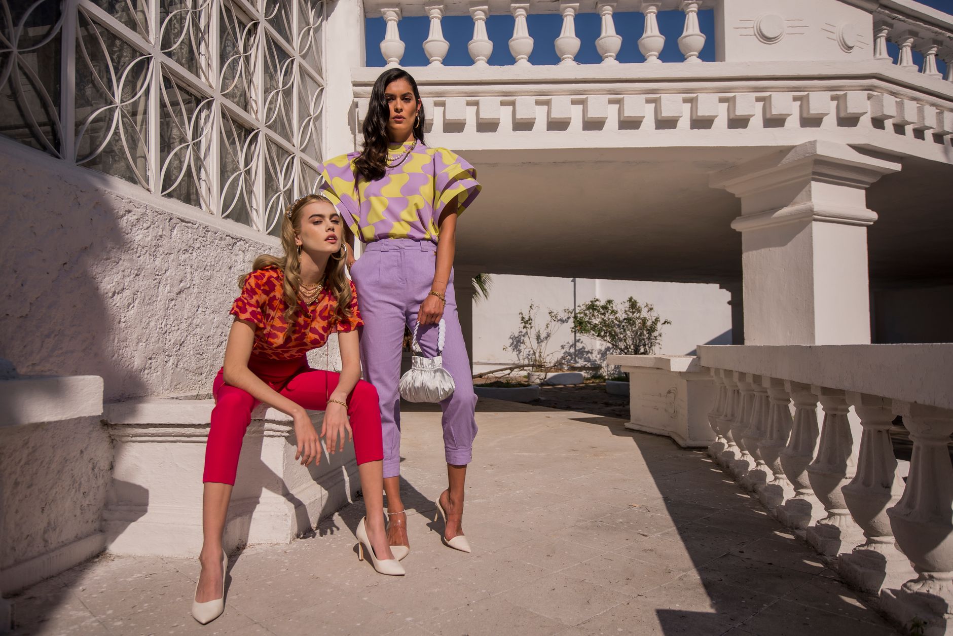 Two fashionable women posing outdoors in vibrant outfits, showcasing modern style.