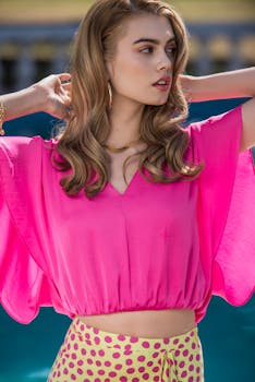 Trendy fashion model in bright pink top enjoying a sunny day outside.