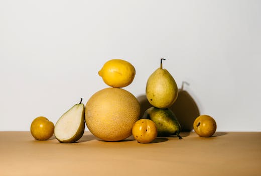 A collection of fresh pears, melon, and lemon creatively arranged on a minimalist background.