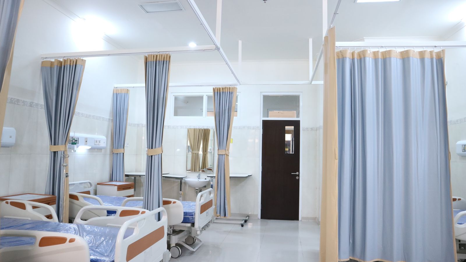Clean and modern hospital ward with beds and privacy curtains in Surabaya, Indonesia.