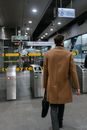 A Person in Brown Coat Holding a Briefcase Walking Towards the Ticket Gate