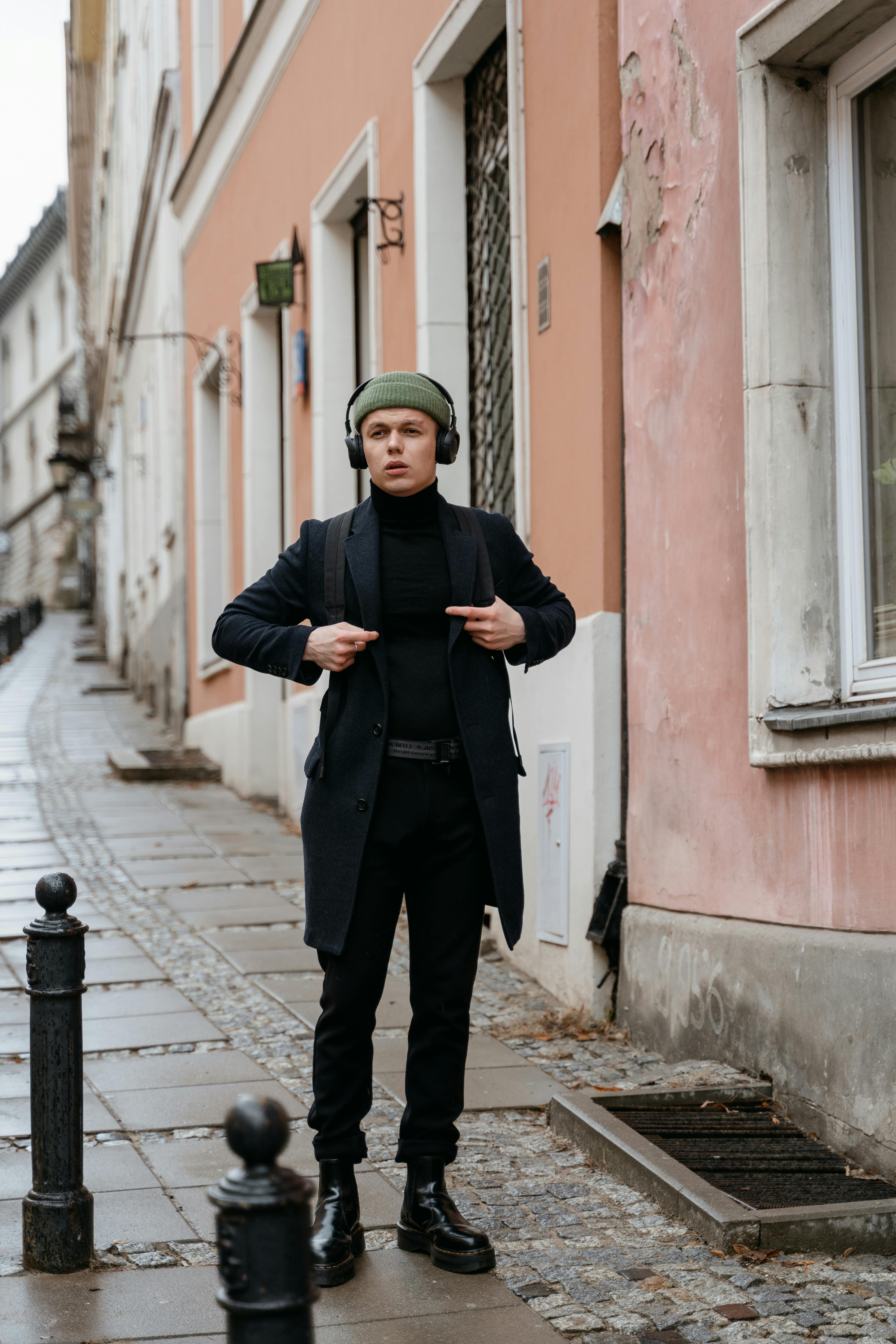 Young adult wearing headphones, standing on a cobblestone street, embracing urban style.