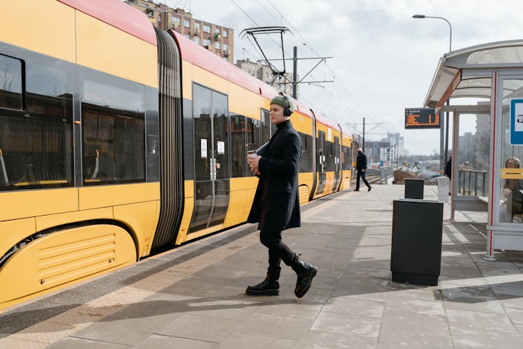 A Man In Black Coat With A Headphones Walking Towards The Train