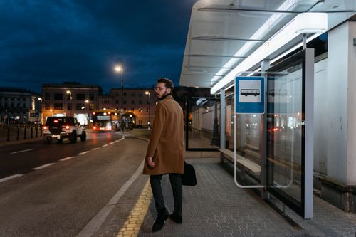 Free Man in coat waits at a bus stop on a city street at night. Stock Photo
