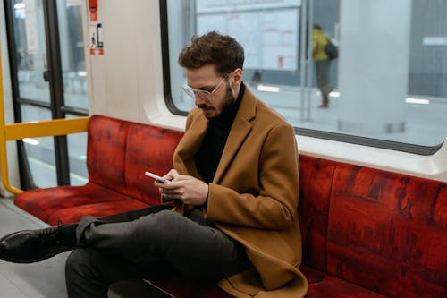 Photo of a Passenger in a Brown Coat Using His Cell Phone
