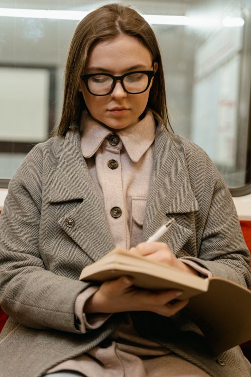 Free Young woman with eyeglasses writes in a notebook while traveling on public transport. Stock Photo