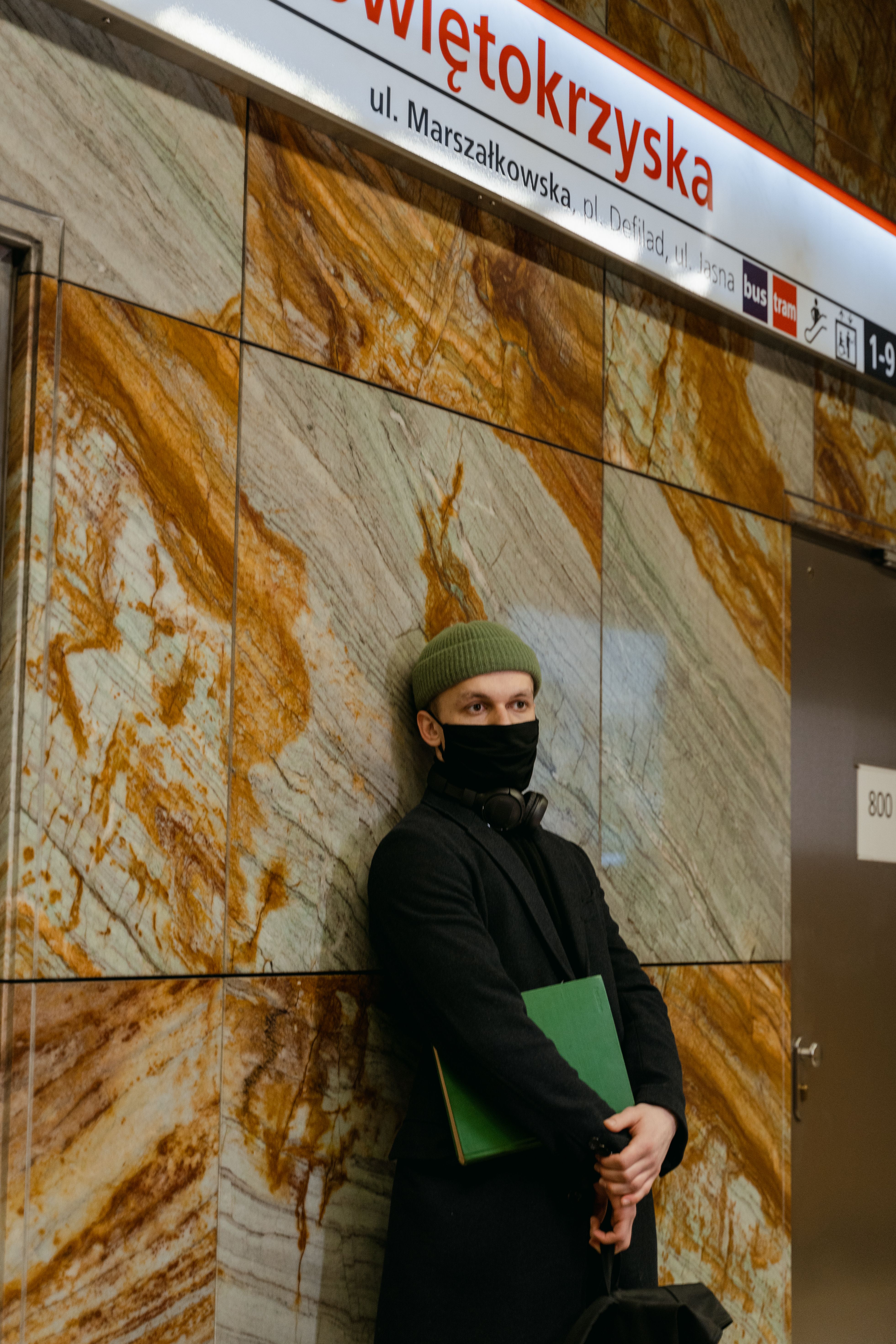 Man in winter clothing stands at Swietokrzyska metro, Warsaw, holding a book.