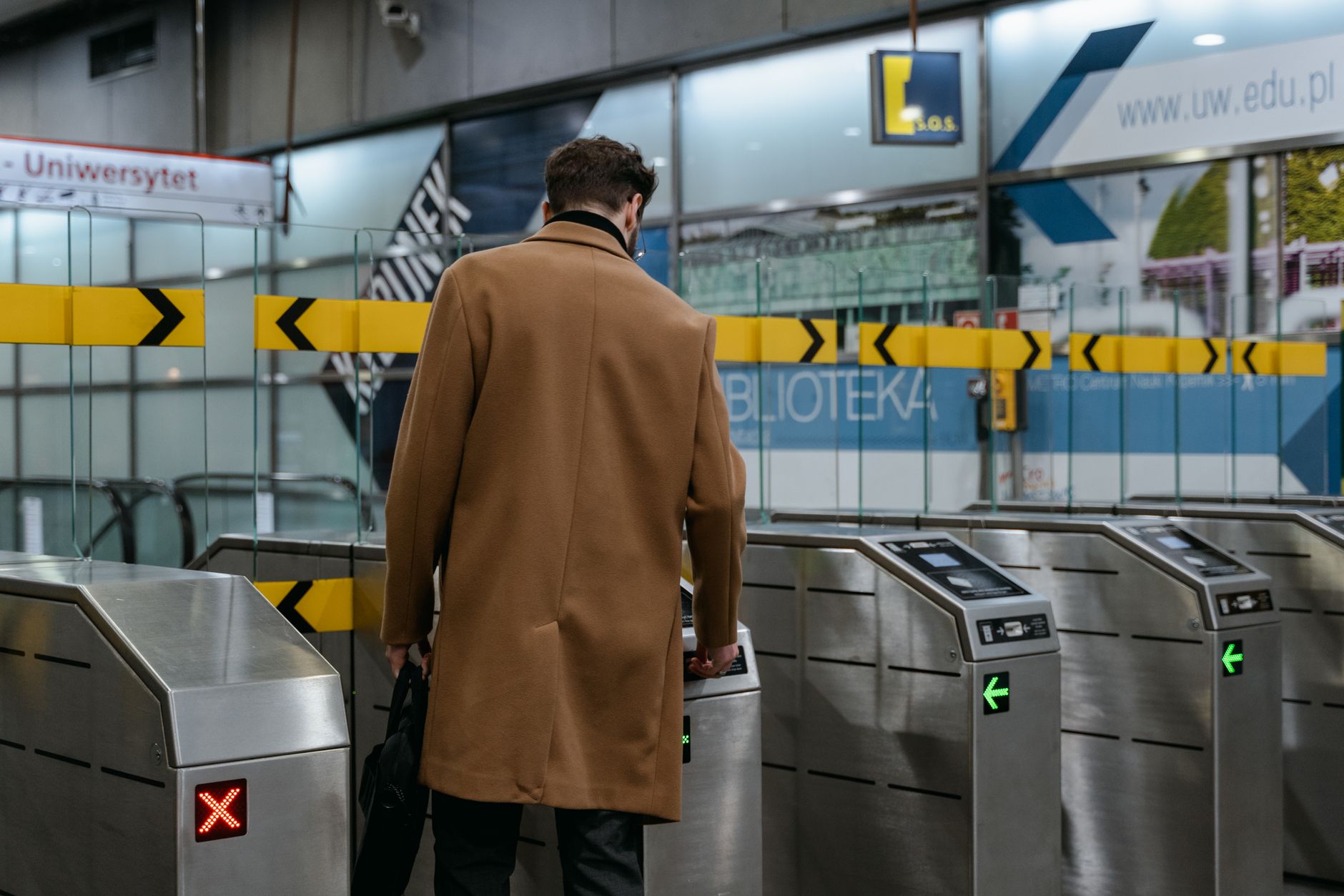 A commuter in a brown coat enters a metro station through ticket barriers.
