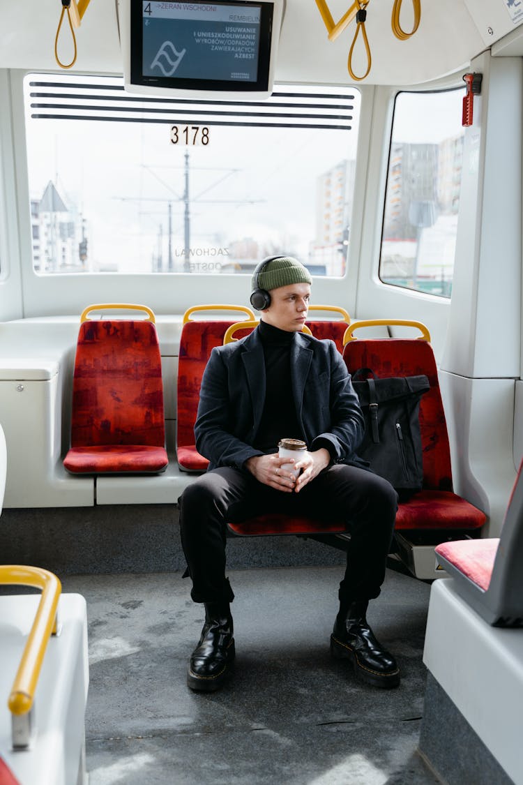 A Man Using Headphones Sitting On A Train Seat Holding A Cup Of Coffee