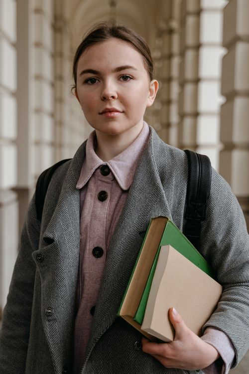 Free Portrait of a young woman with books in a classic architectural hallway. Stock Photo