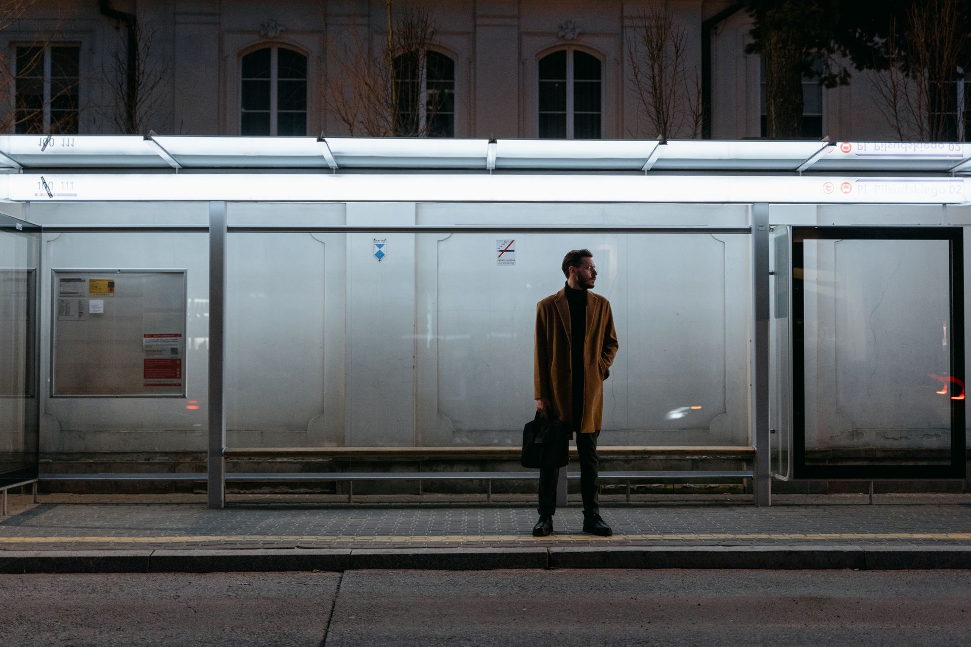 A Man in Brown Coat Standing on a Waiting Shed